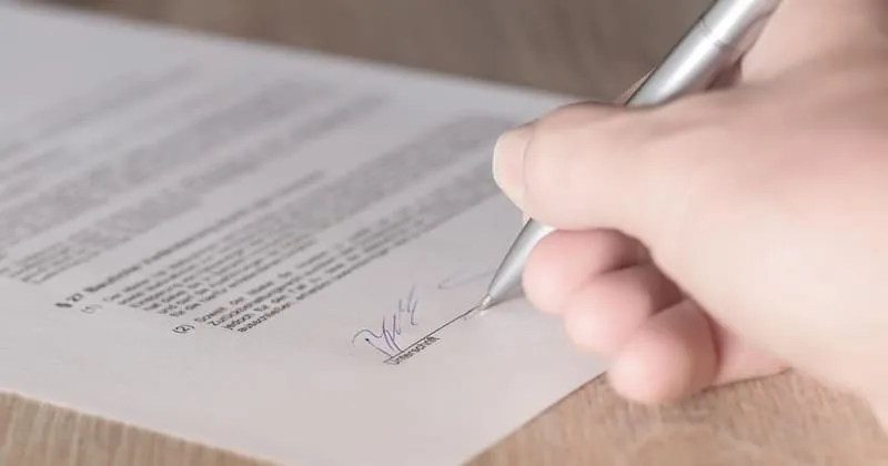 契約書の署名欄にペン先を添える手元