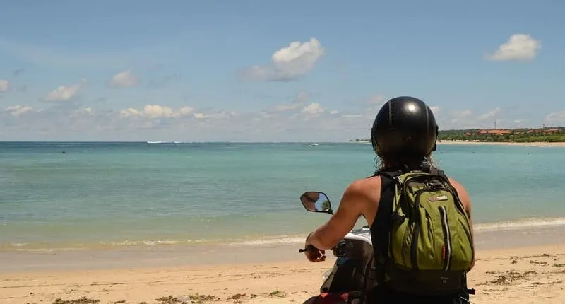 海辺の道をスクーターで走る人物の後ろ姿