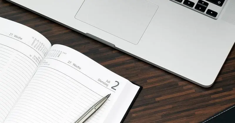 開いたダイアリーにペンを置いたノートPCの隣