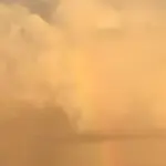 厚い雲の壁に立つ淡い虹の一筋