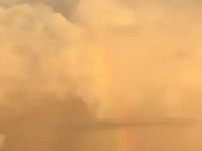 厚い雲の壁に立つ淡い虹の一筋