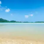 浅瀬の砂浜と静かな海、遠くに低い山並み