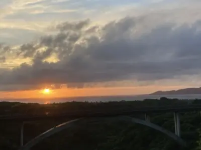 夕焼け空の下、森の上にアーチ橋と海が見える石垣島の風景