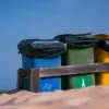 青空の下 砂地に並ぶ色分けごみ箱