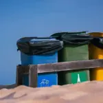 青空の下 砂地に並ぶ色分けごみ箱