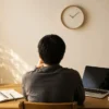 時計のある部屋で、机に向かいながら作業の入口を考える人の後ろ姿